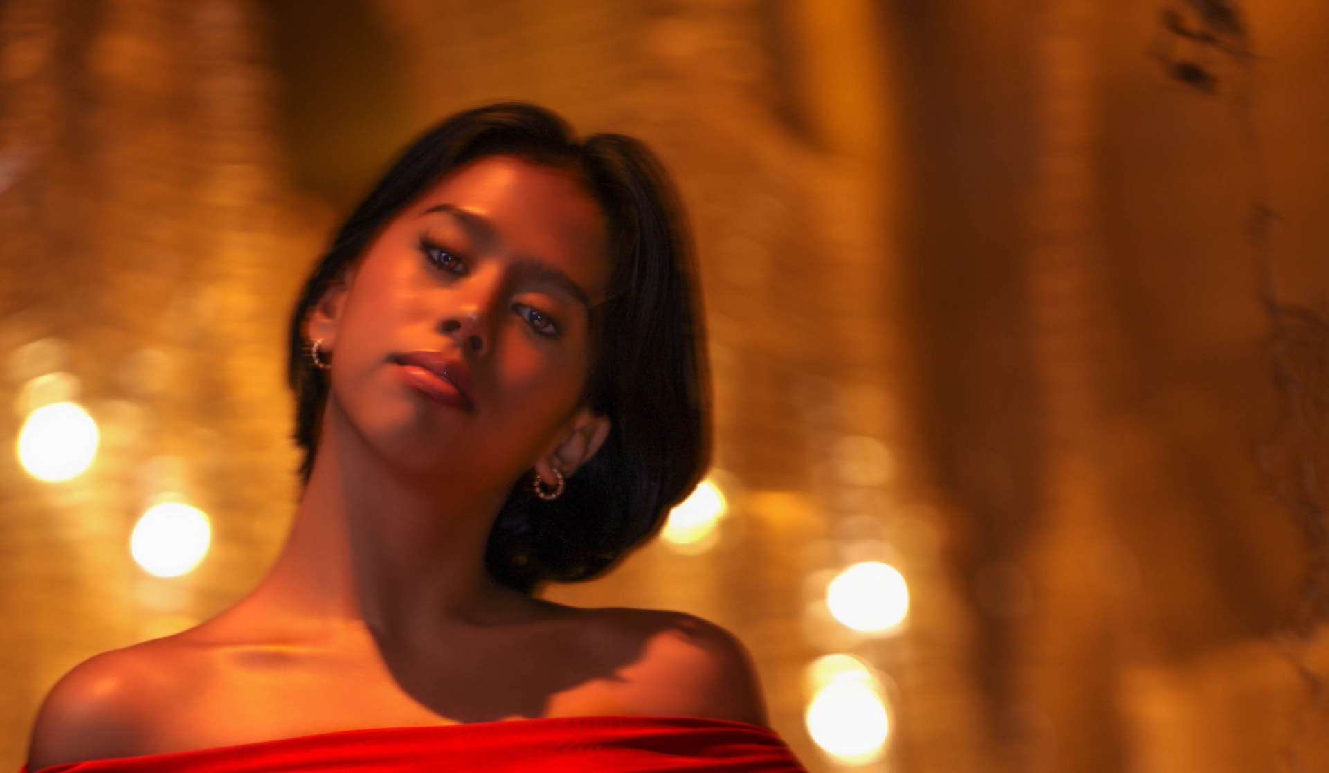 Close portrait tilted against warm gold bokeh, bare shoulder in red