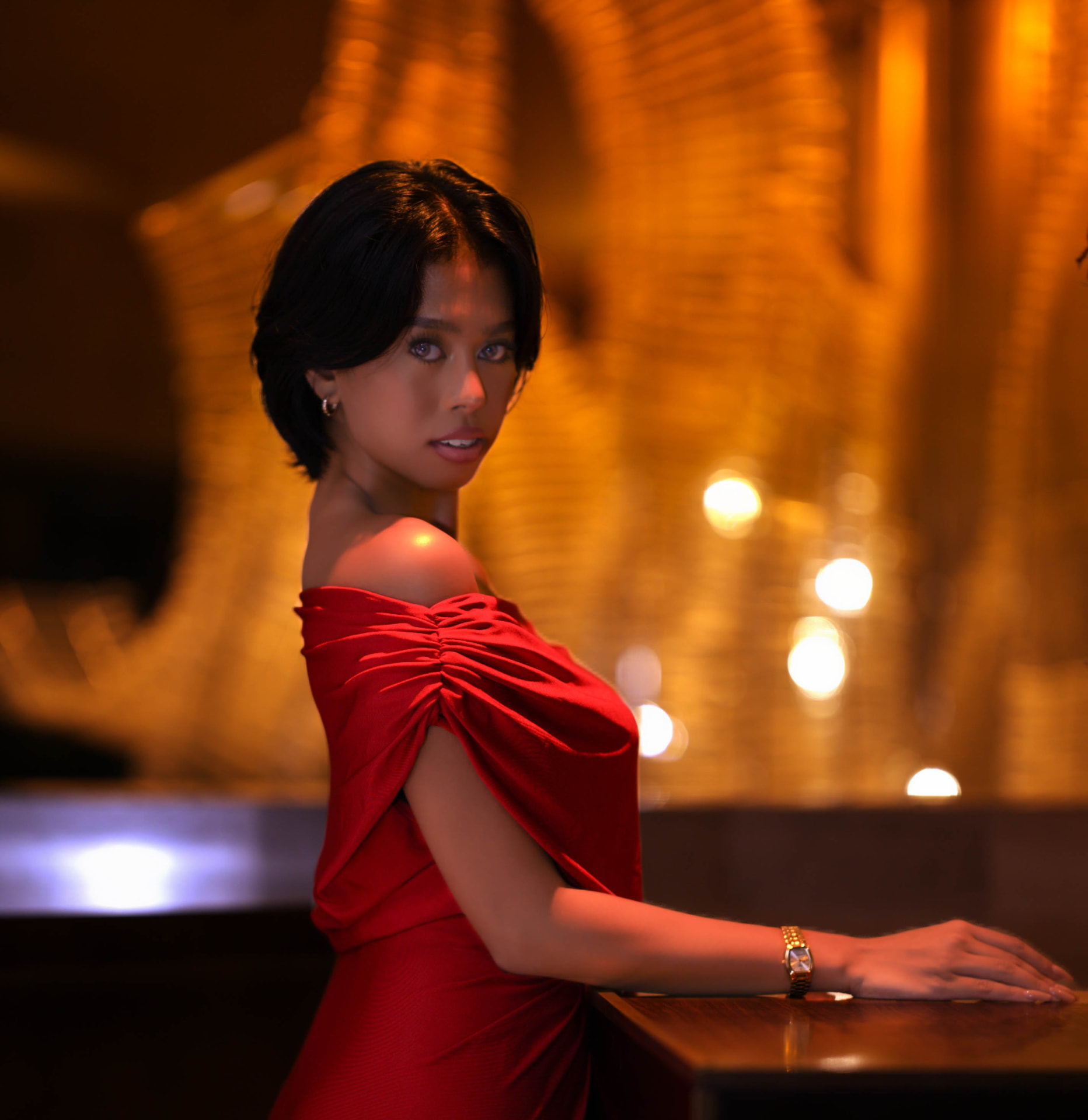 Portrait in a red off-shoulder dress at a bar, turned to the lens against gold light