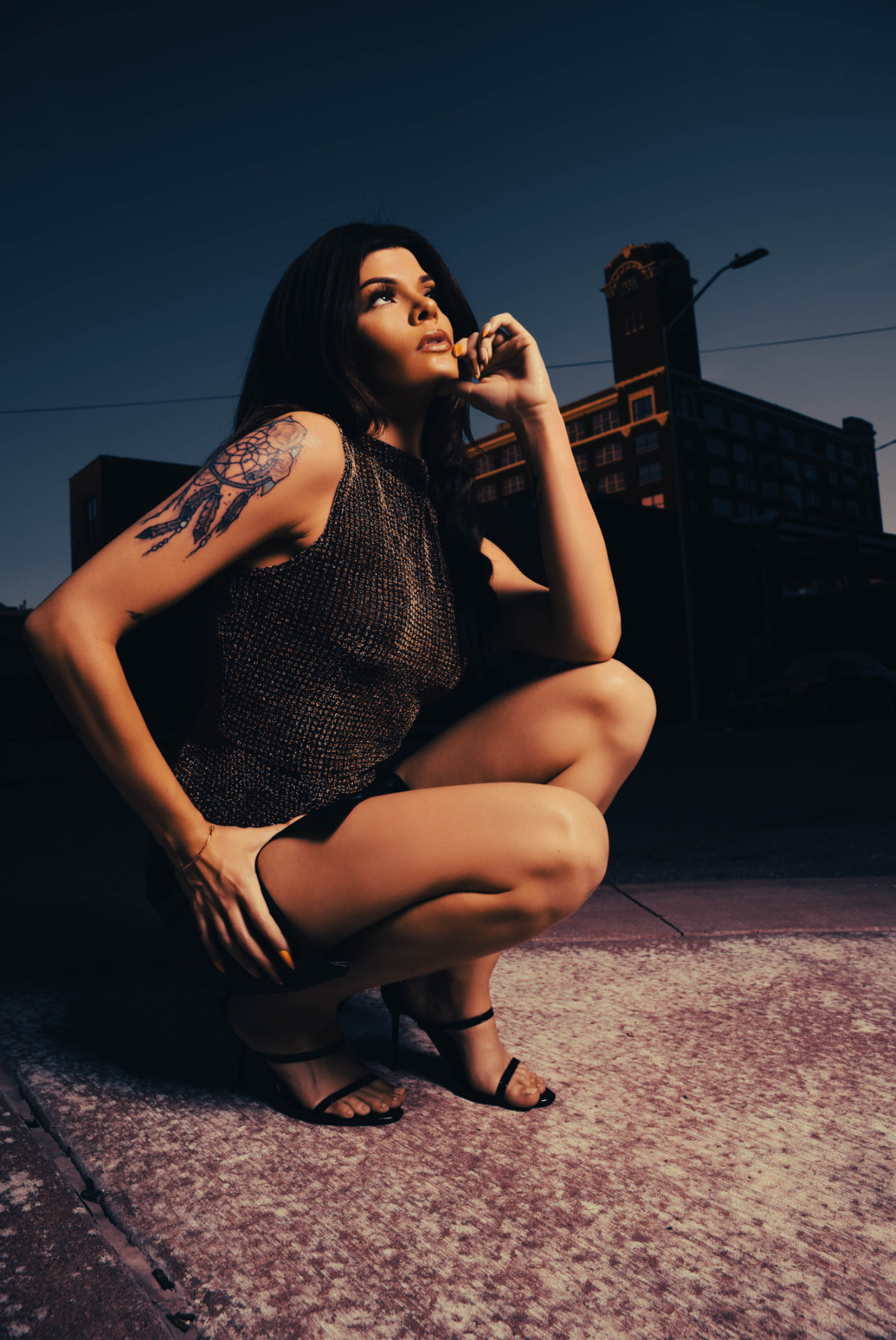 Portrait crouched on a Kansas City street at dusk, clock tower behind against a deep blue sky